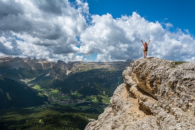 hiker standing on mountain looking at green valley below