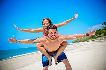 girl on mans back on beach with arms open wide