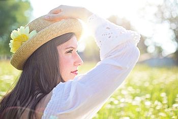 woman wearing hat in field with sun behind her